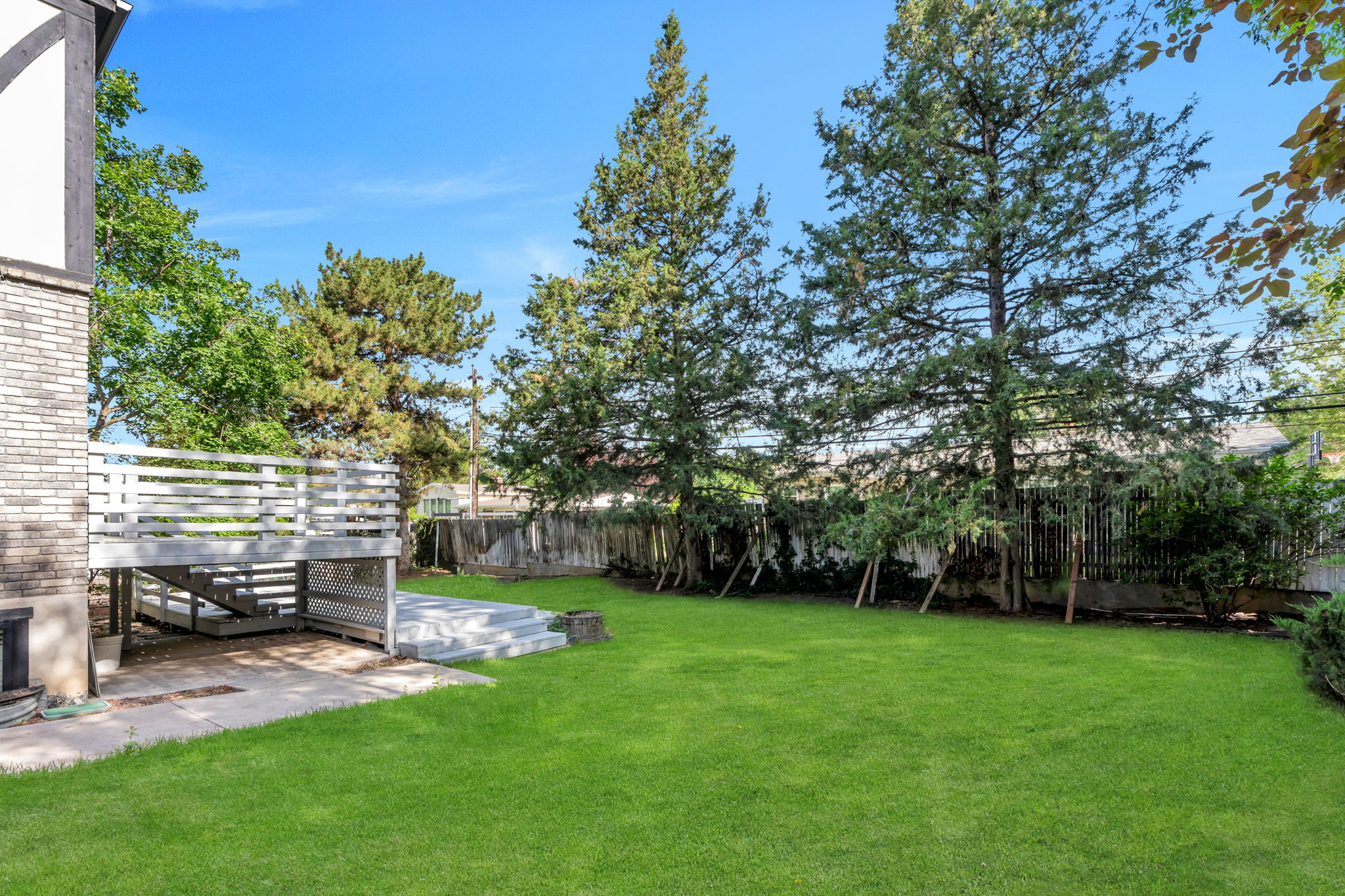 Expansive backyard featuring a lush lawn, multi-level wooden deck, stone patio, and mature trees providing natural screening
