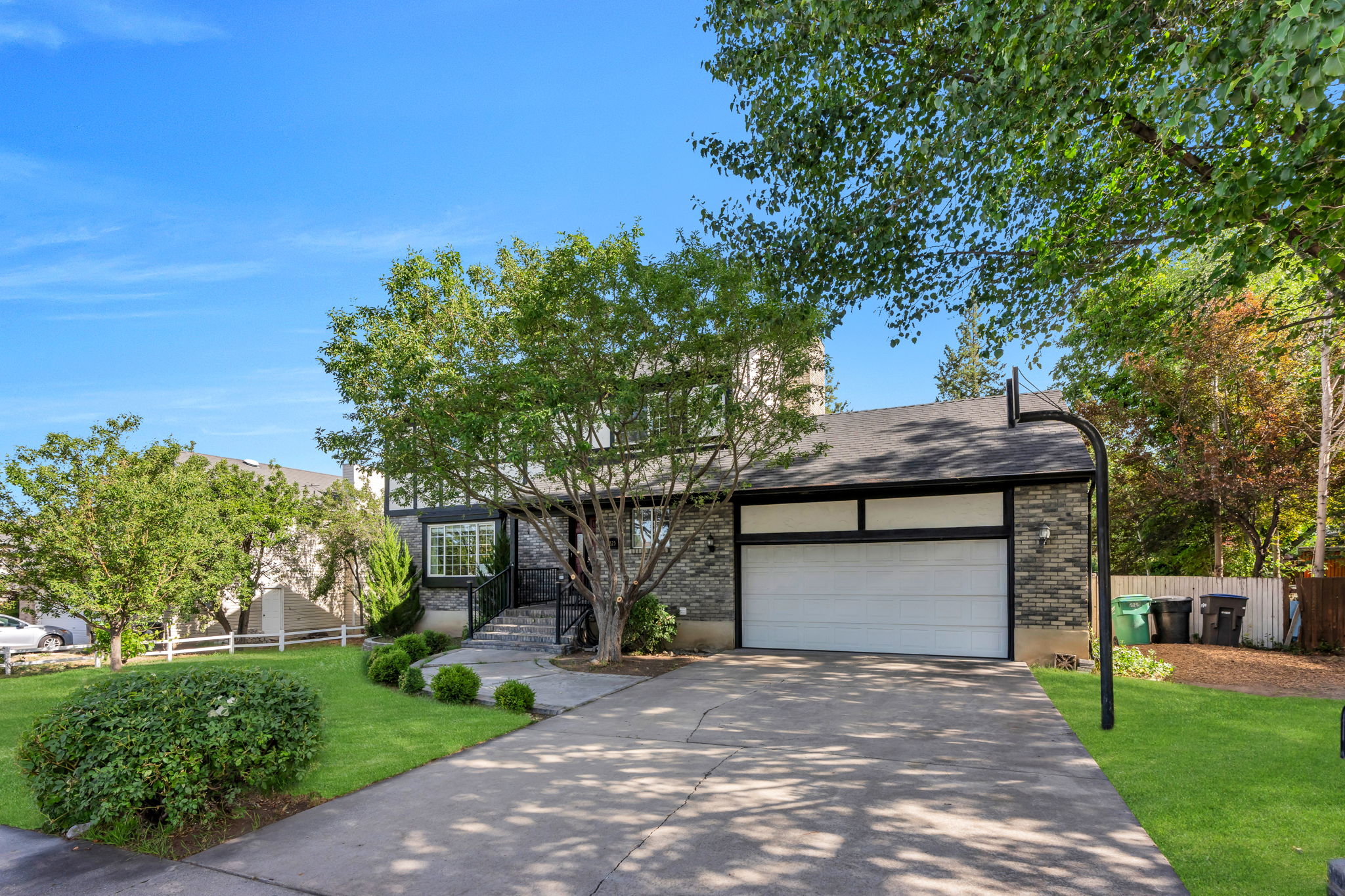 Stone facade residence featuring a two-car garage, mature trees, and a concrete driveway