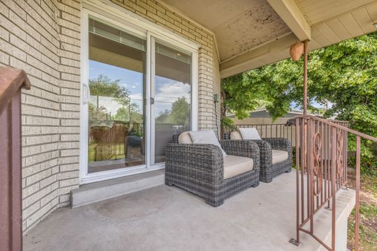Covered concrete patio featuring a sliding glass door, brick exterior wall, and decorative metal railing
