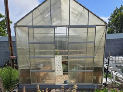 Gable-roof greenhouse featuring translucent paneling and a metal frame