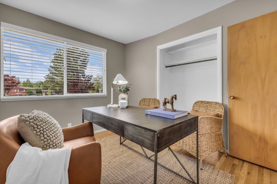 Room featuring a large window with white blinds, neutral wall paint, and wood-finish flooring