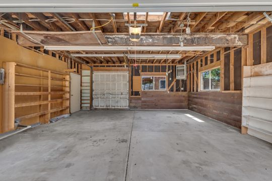 Expansive garage space with exposed wood framing, concrete flooring, built-in shelving, two windows, and an overhead garage door