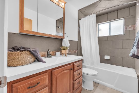 Bathroom featuring a wood-finish vanity with an integrated sink, a matching medicine cabinet, and a bathtub with a tiled surround