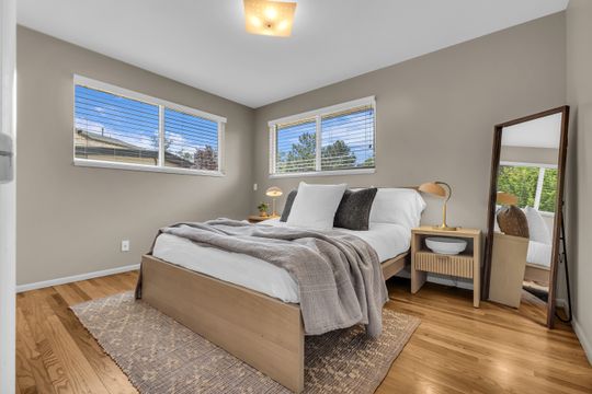 Bedroom featuring wood-finish flooring, neutral wall tones, and two large windows with blinds