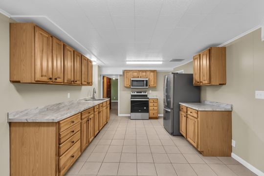 Kitchen featuring extensive cabinetry, tile flooring, stainless steel appliances, a double basin sink, and ample countertop space