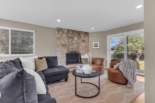 Stone-faced fireplace with a black iron screen, recessed lighting, wood-finish flooring, a white-framed window, and a sliding glass door