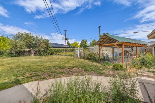 Expansive backyard featuring a large grassy area, mature tree, concrete patio, and a covered structure with a metal roof