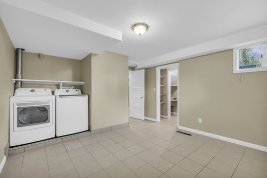 Spacious utility area featuring neutral-toned tile flooring, light-colored walls, and a visible built-in storage closet