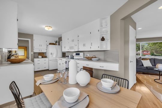 Eat-in kitchen featuring white cabinetry, light countertops, wood-finish flooring, and an open doorway to another room