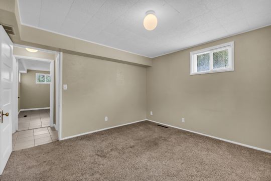 Spacious room featuring neutral-toned walls, plush carpeting, and a white-framed window