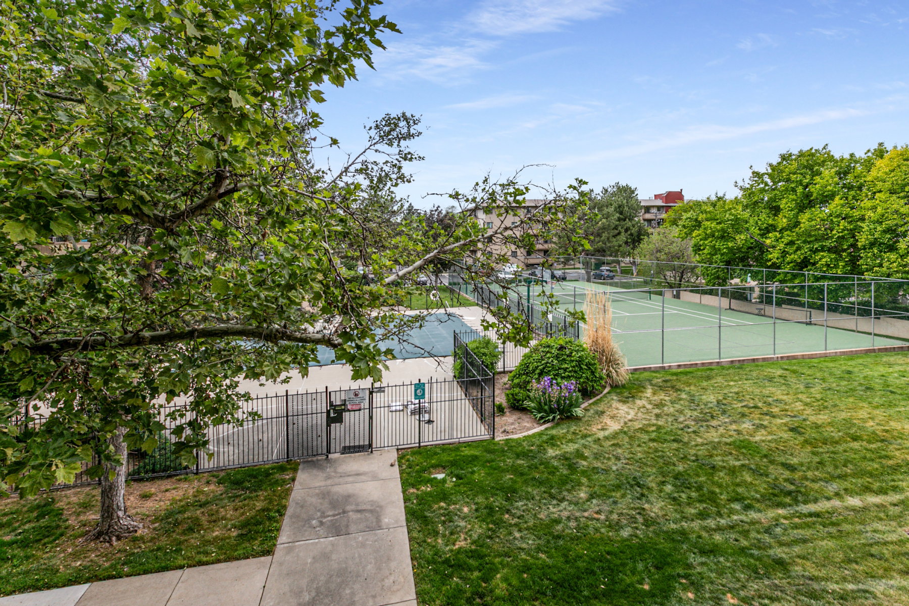 Spacious outdoor area featuring a tennis court with chain-link fencing, a second court, and surrounding green space