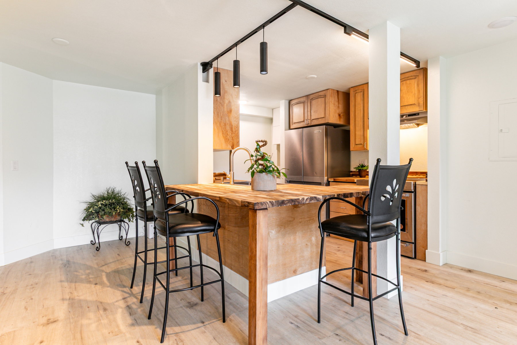 Kitchenette featuring a wood-finish island with integrated sink, stainless steel refrigerator, wood cabinetry, and track lighting