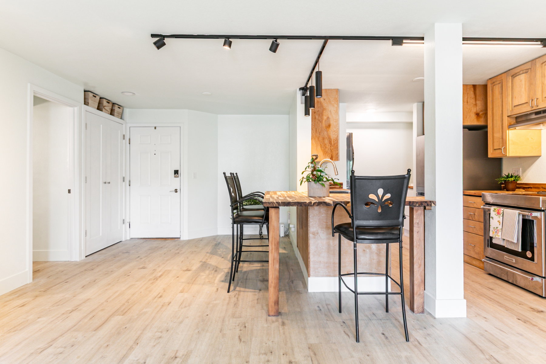 Open concept living area featuring light wood-finish flooring, track lighting, and a white paneled entry door