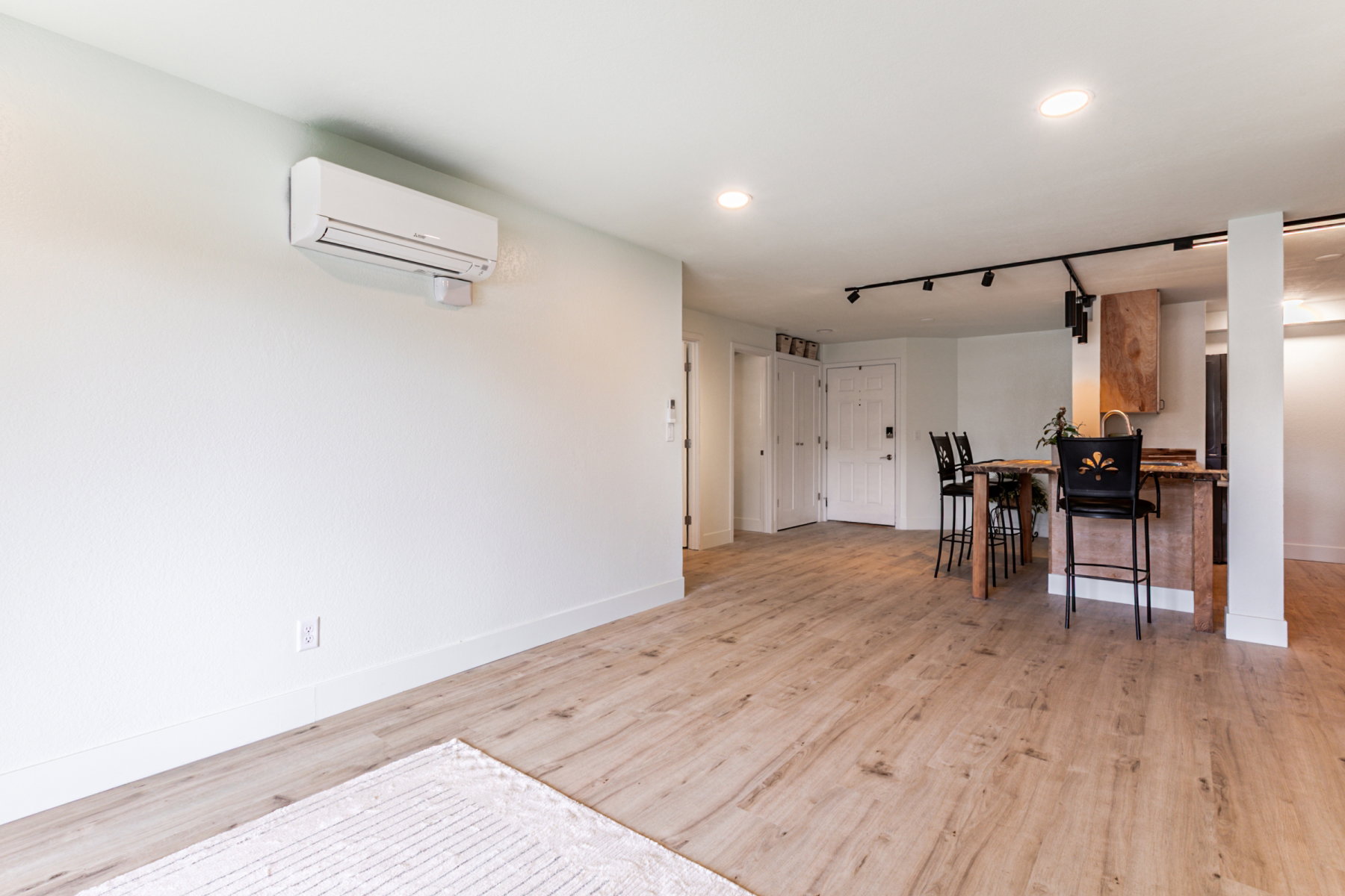 Open-concept living area featuring wood-finish flooring, a wall-mounted mini-split system, recessed lighting, and track lighting