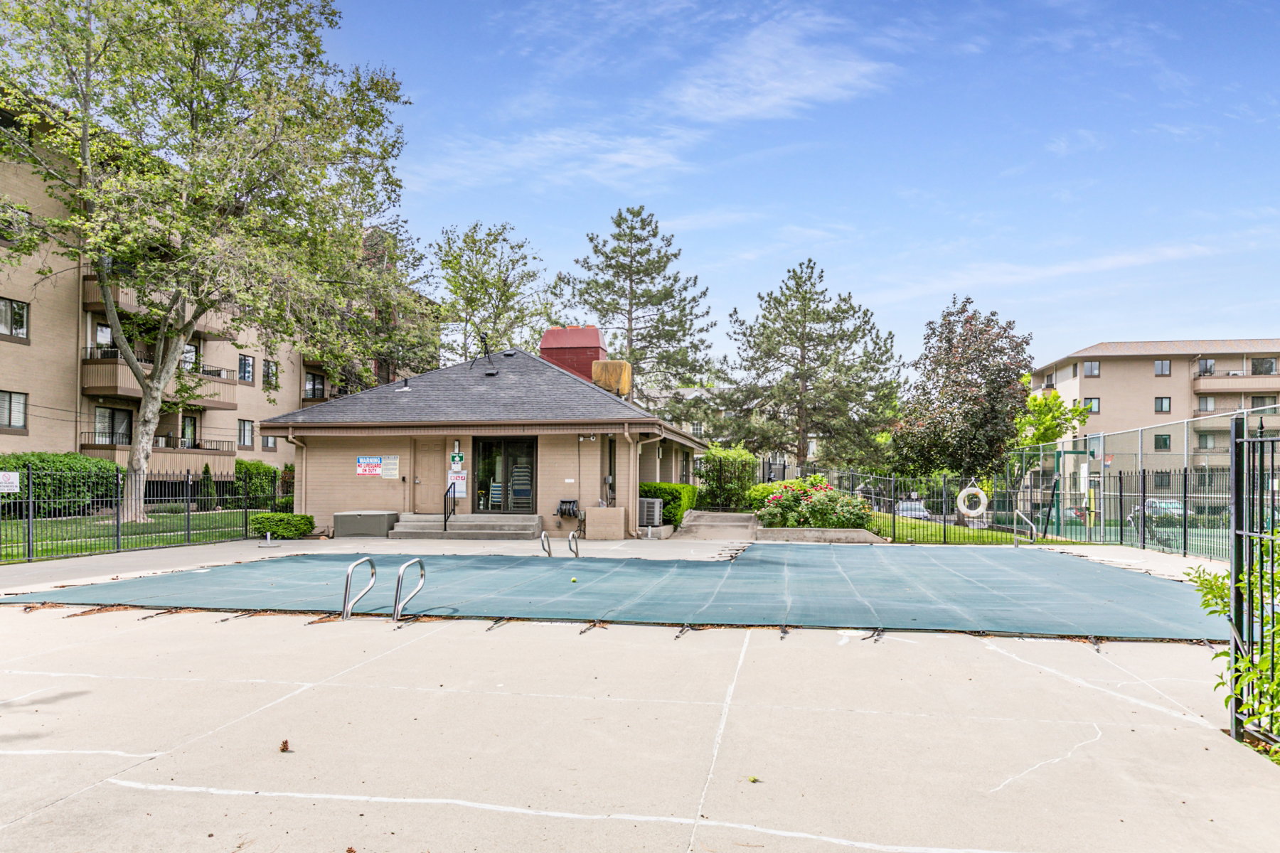 Outdoor pool with a protective cover, surrounded by a concrete deck and a black metal fence