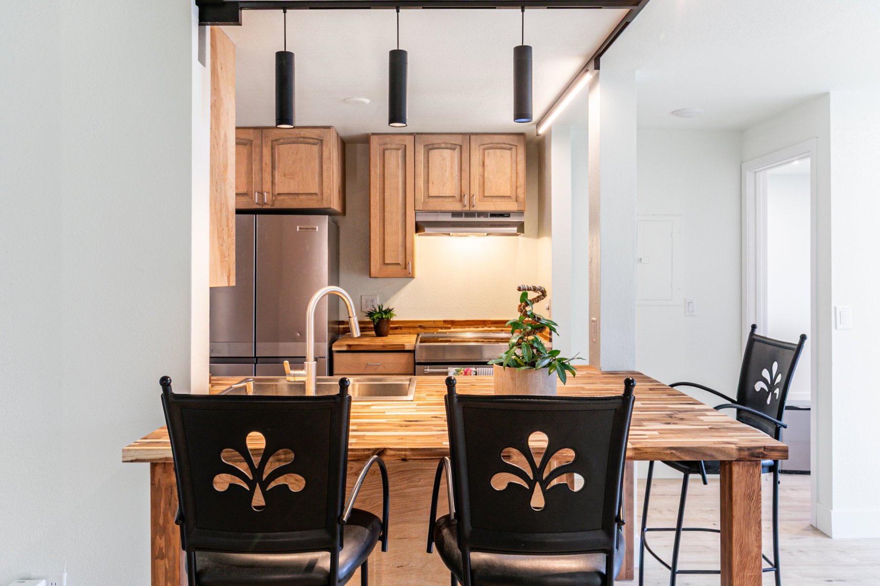 Kitchen area featuring a wood-finish peninsula with seating, stainless steel appliances, natural wood cabinetry, pendant lighting, and a gooseneck faucet