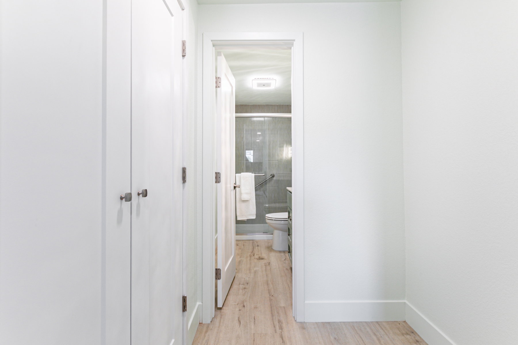 Recessed lighting illuminates a bathroom with a glass-enclosed shower, wall-mounted grab bars, and a white toilet