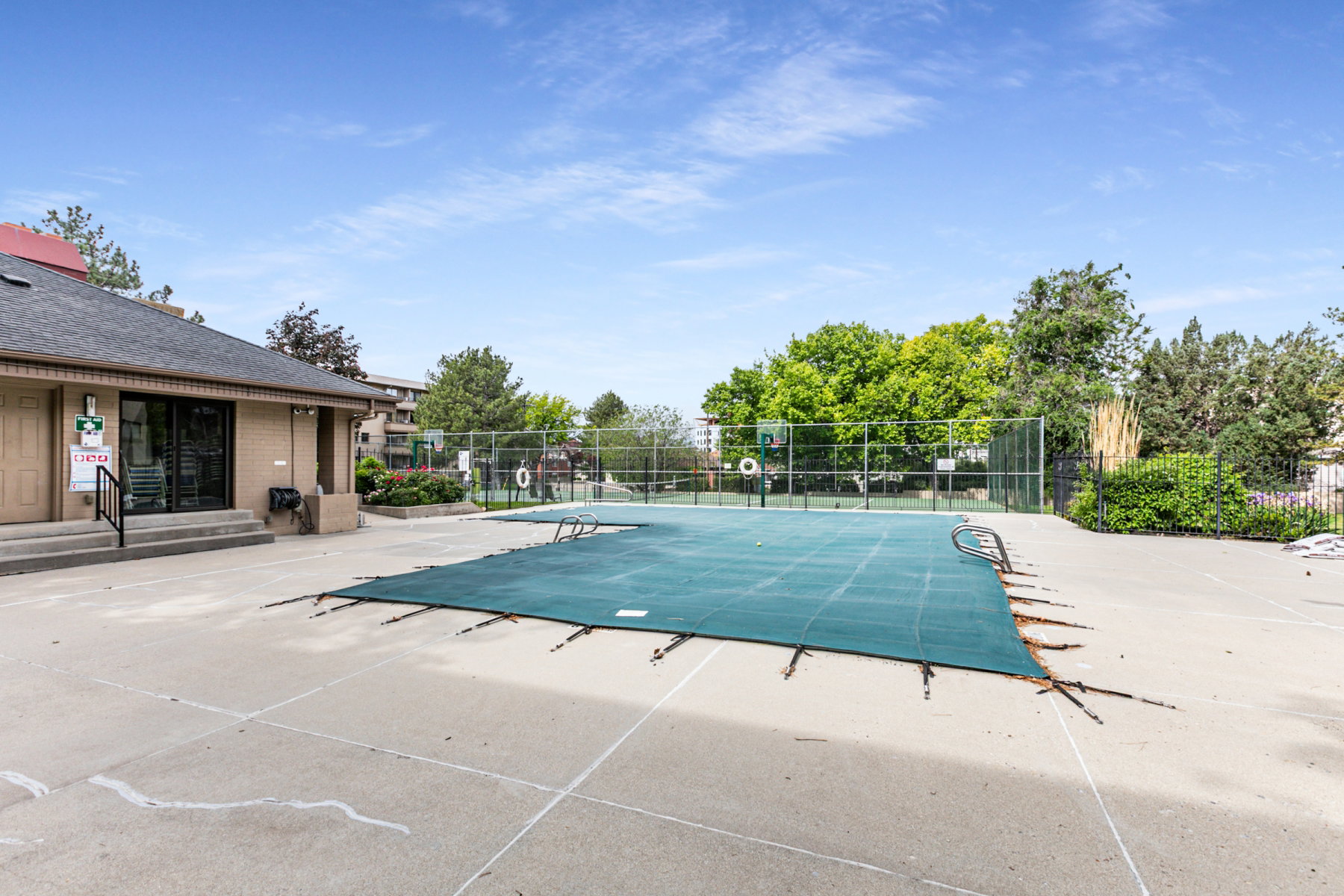 Outdoor swimming pool with a protective cover, surrounded by a concrete deck and a perimeter fence