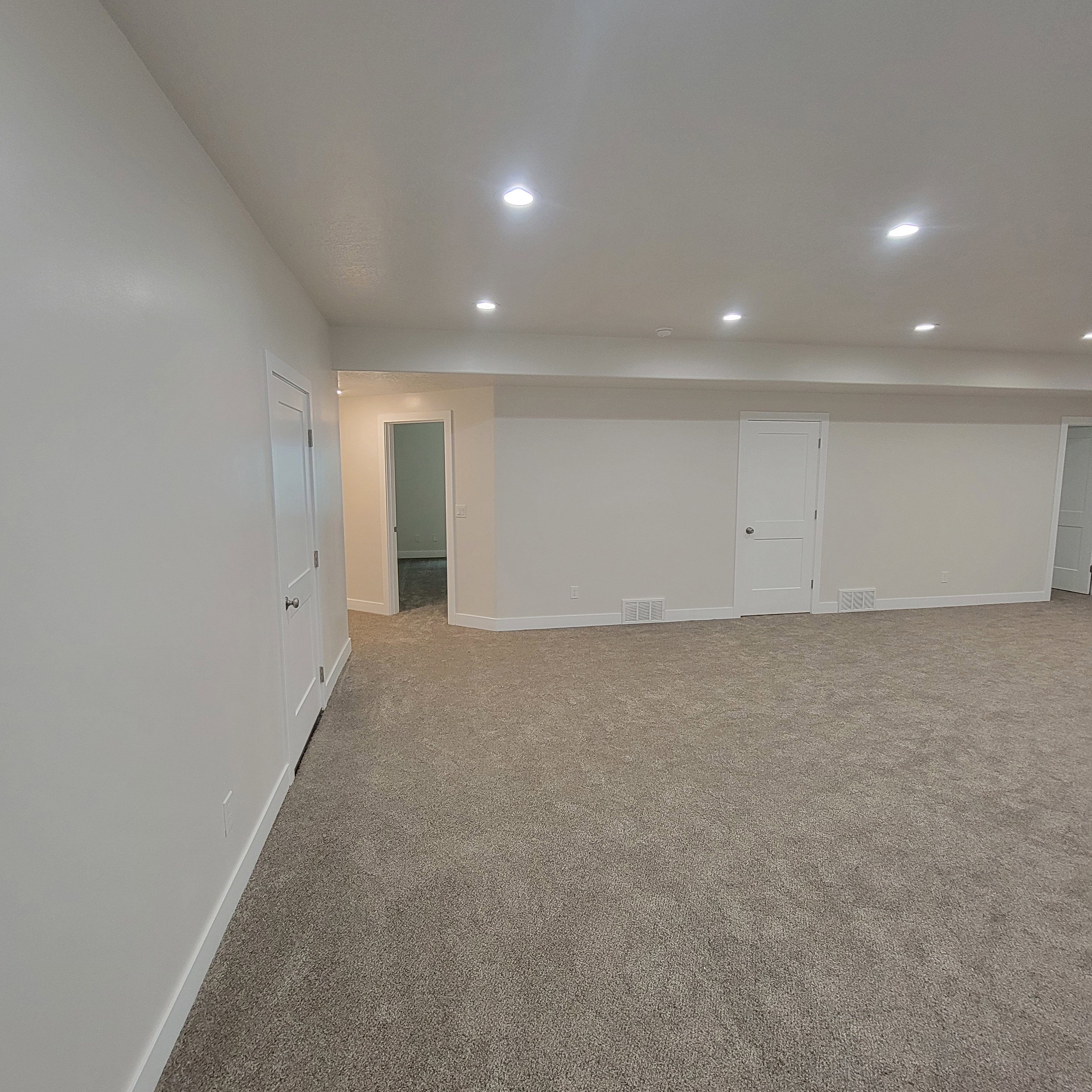 Expansive carpeted area featuring recessed lighting, white walls, and multiple door access points