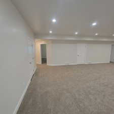 Expansive carpeted area featuring recessed lighting, white walls, and multiple door access points