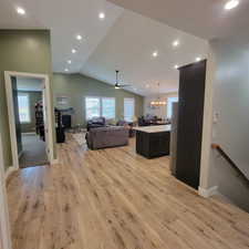 Spacious open-concept living area featuring wood-finish flooring, vaulted ceilings with recessed lighting, and a kitchen island with a light-toned countertop