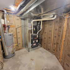 Utility area featuring a water heater, furnace, insulated walls, exposed ductwork, and concrete flooring