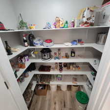 Walk-in pantry featuring extensive U-shaped shelving, light wood-finish flooring, and white walls