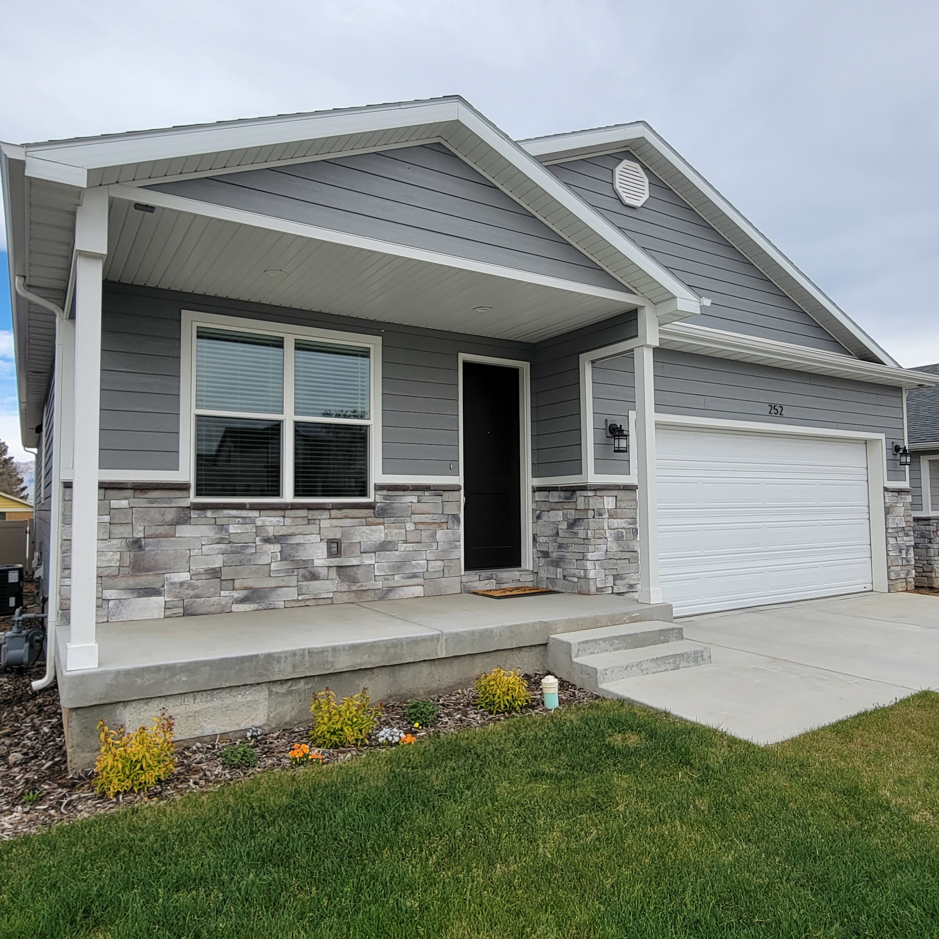 Exterior featuring gray horizontal siding, a stone veneer facade, a covered front porch, a dark entry door, and an attached white garage door
