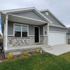 Exterior featuring gray horizontal siding, a stone veneer facade, a covered front porch, a dark entry door, and an attached white garage door
