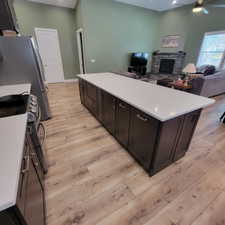 Open-concept kitchen and living area featuring a large center island with a light-toned countertop, wood-finish flooring, and vaulted ceilings
