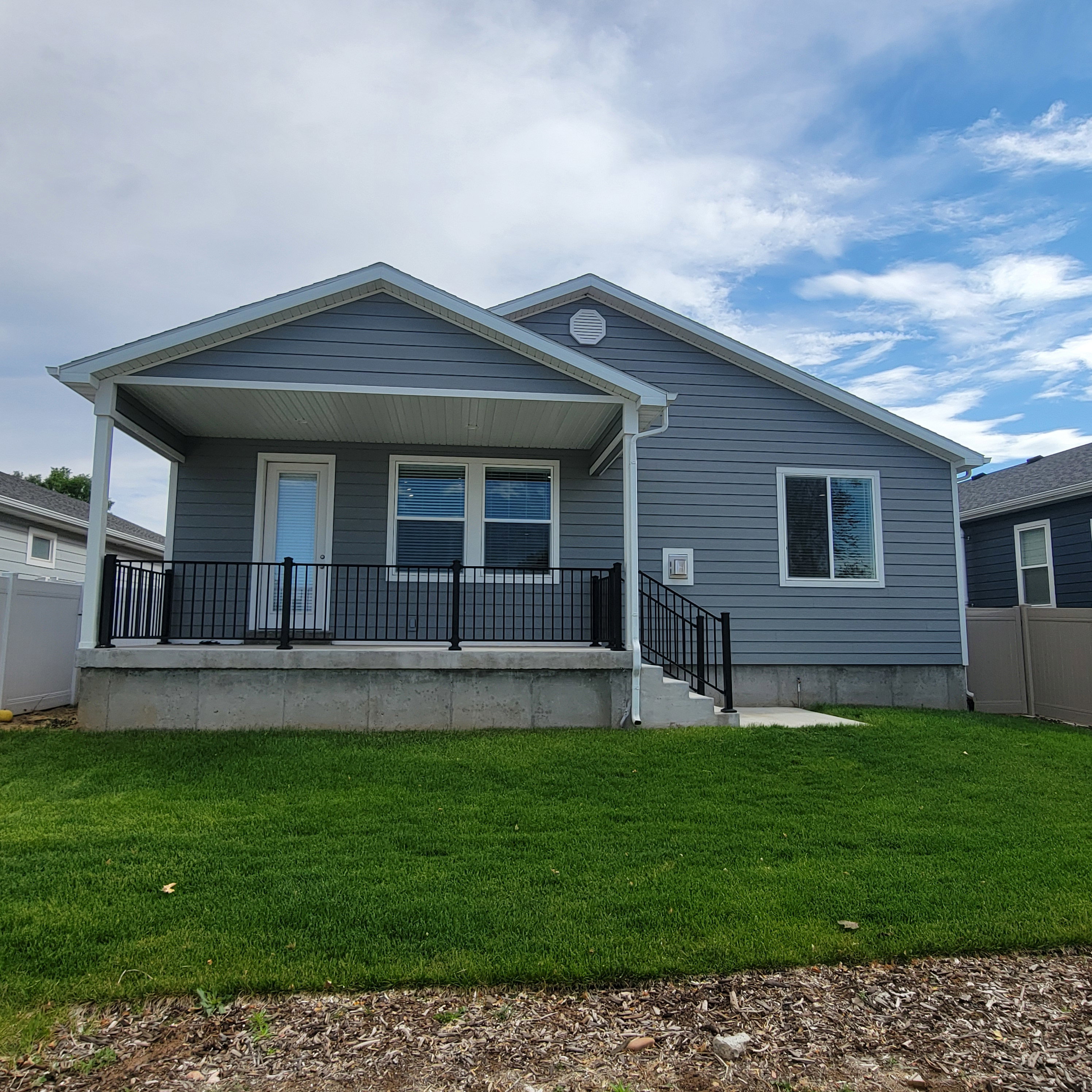 Rear exterior featuring a covered patio with black metal railings, gray siding, white trim, and a manicured lawn