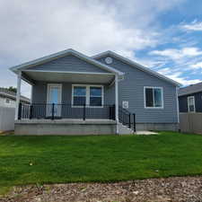 Rear exterior featuring a covered patio with black metal railings, gray siding, white trim, and a manicured lawn