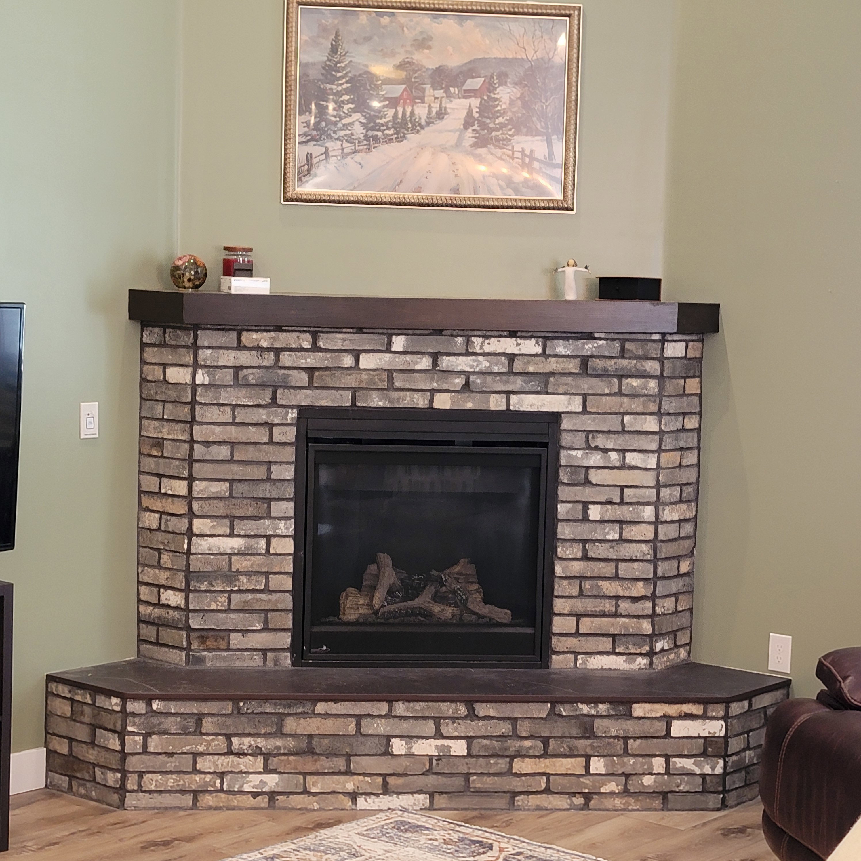 Corner fireplace featuring a brick surround, dark wood-finish mantel, and a dark tile hearth