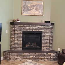Corner fireplace featuring a brick surround, dark wood-finish mantel, and a dark tile hearth