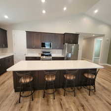 Kitchen featuring an oversized island with white countertop, dark wood cabinetry, stainless steel appliances, and wood-finish flooring