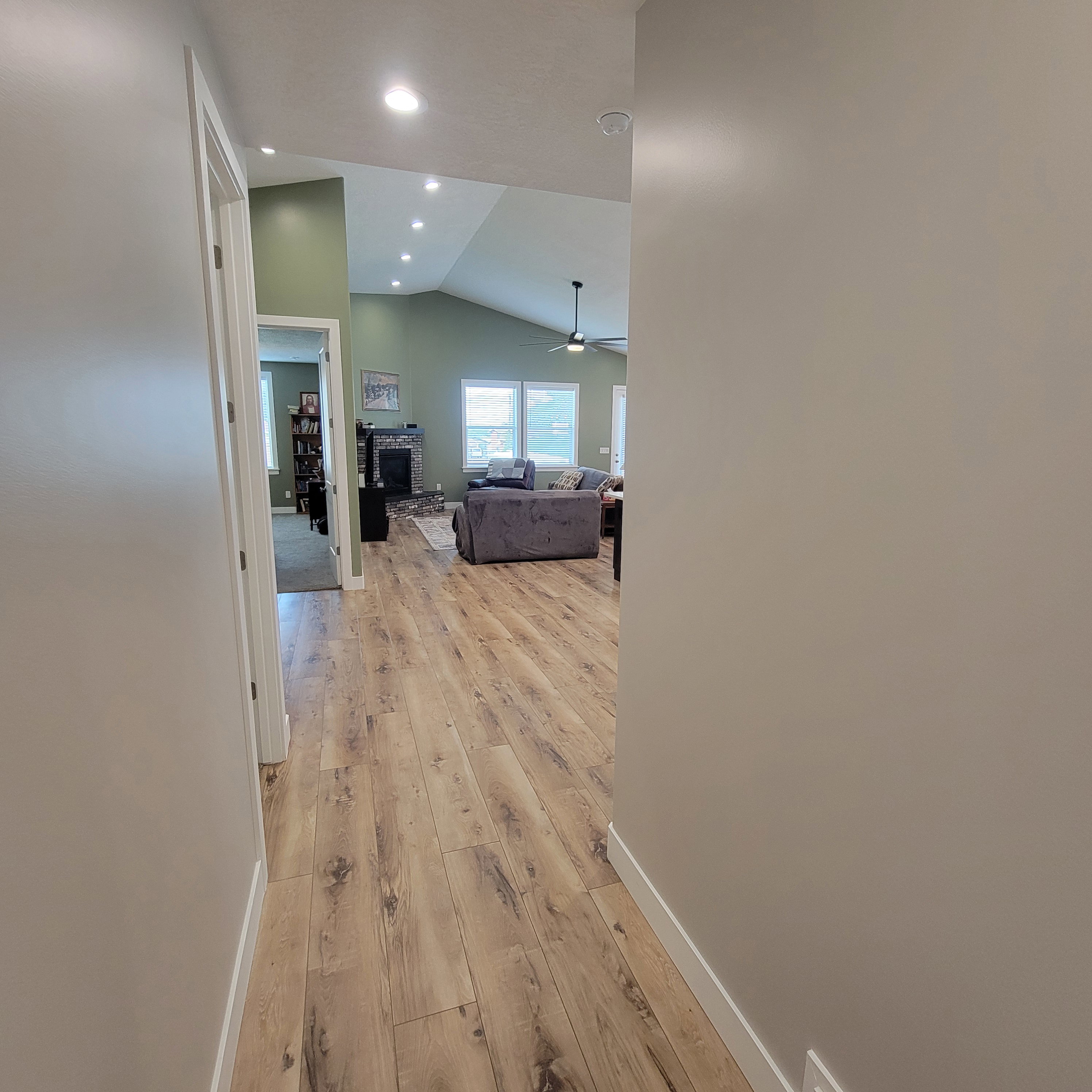Hallway with wood-finish flooring leading to a living area featuring vaulted ceilings, recessed lighting, and a ceiling fan