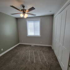 Neutral toned room featuring a ceiling fan with integrated lighting, a window with blinds, and white bi-fold closet doors