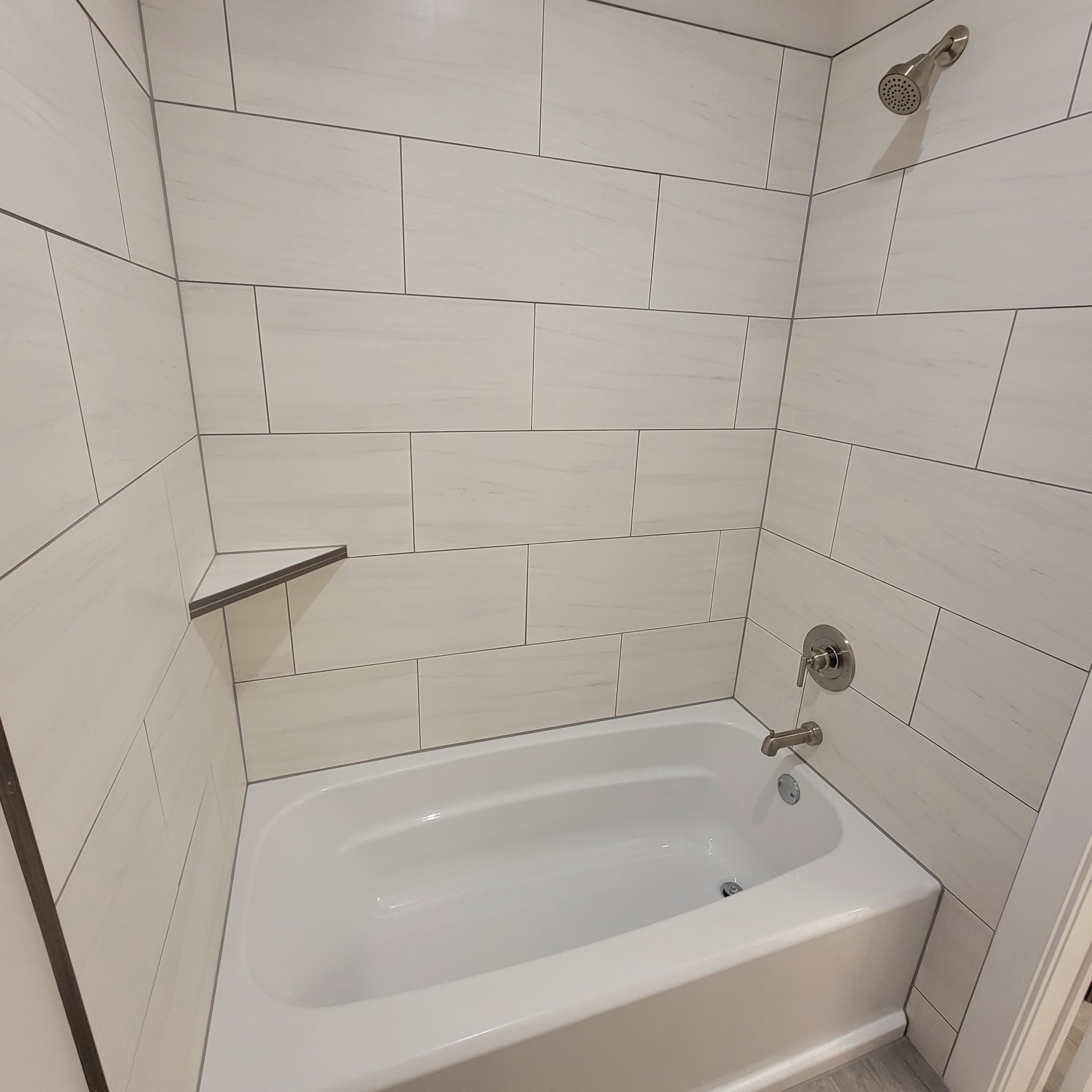 Bathtub with white subway tile surround, corner shelf, and brushed nickel fixtures