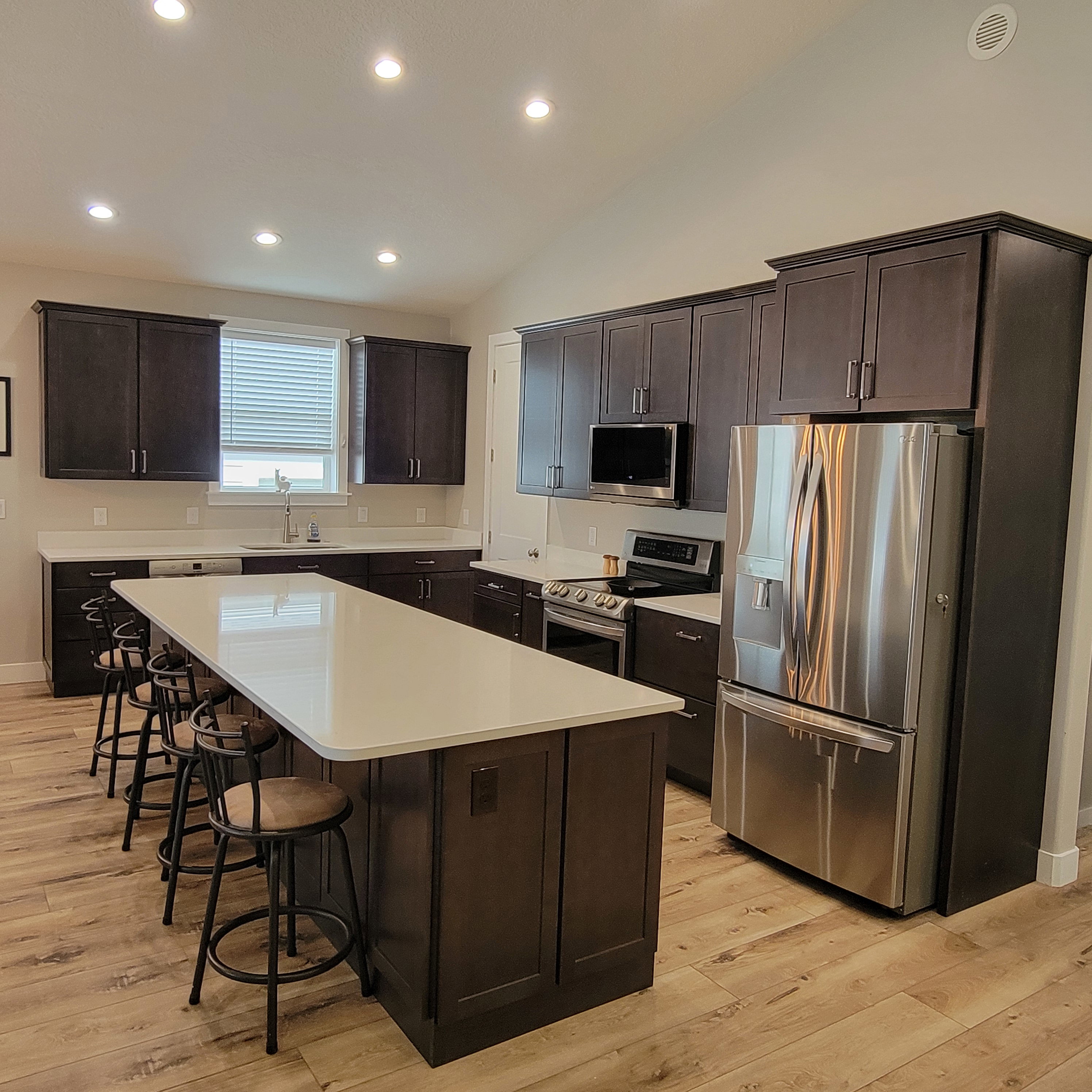Spacious kitchen featuring an expansive island with seating, dark wood cabinetry, light wood-finish flooring, recessed lighting, and stainless steel appliances