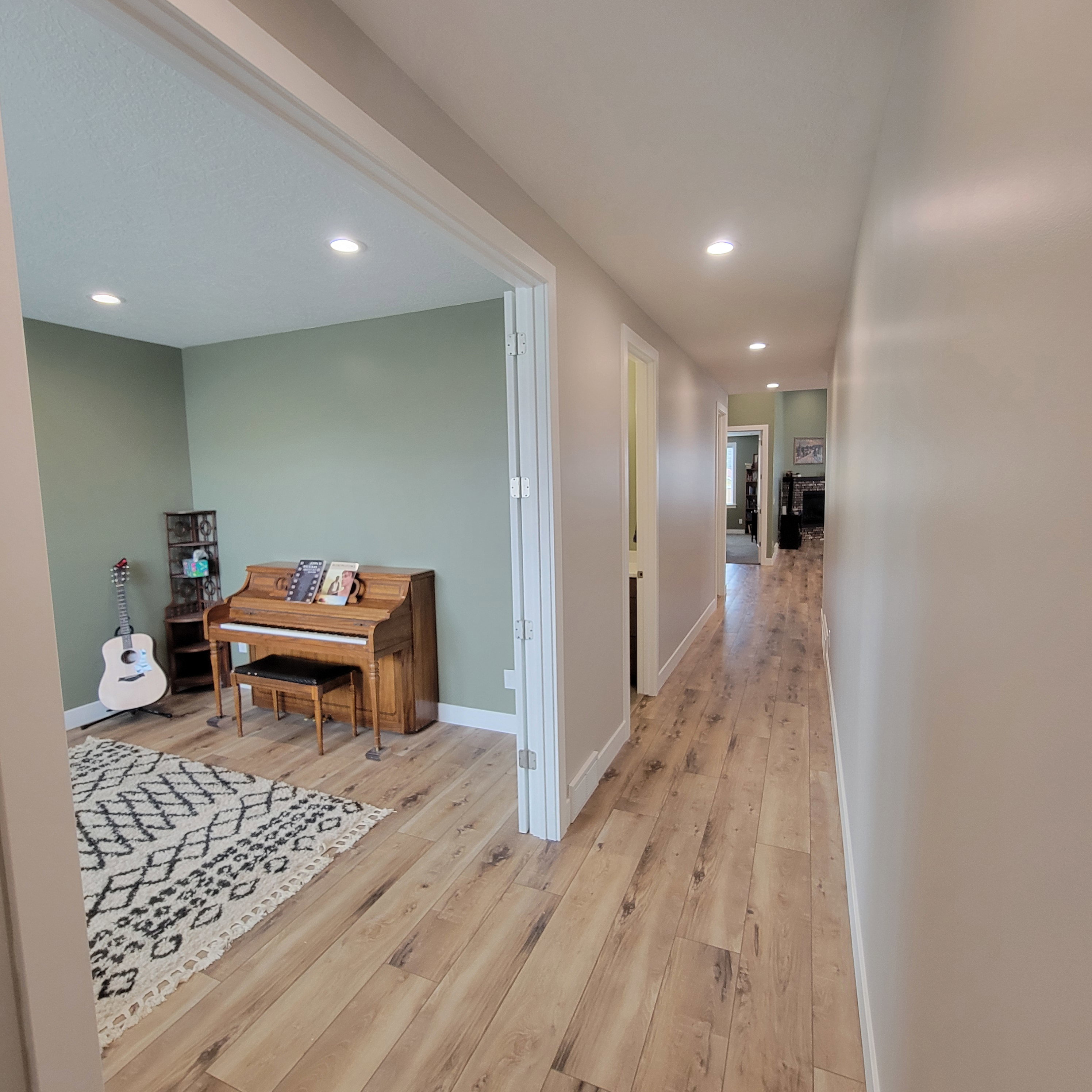 Spacious hallway with light wood-finish flooring extending into an open room featuring recessed lighting and light green walls