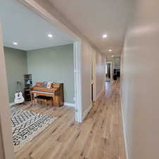Spacious hallway with light wood-finish flooring extending into an open room featuring recessed lighting and light green walls