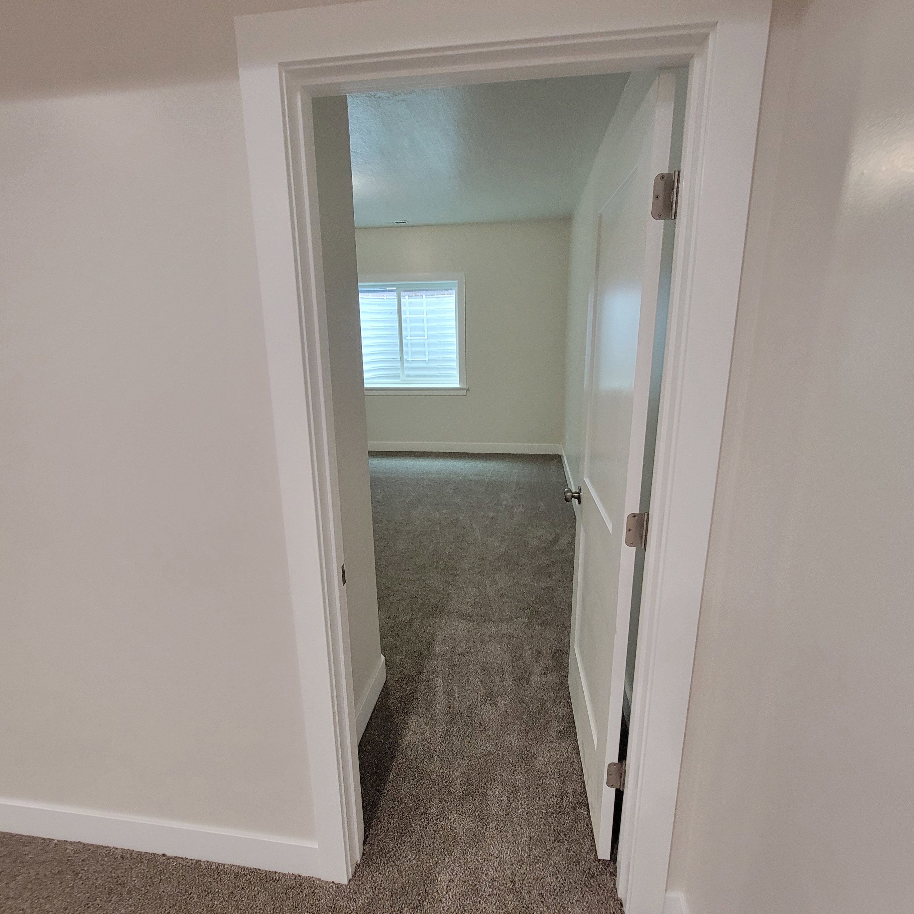 Carpeted room with a white door and trim, featuring a window with horizontal blinds