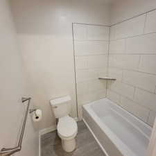 Contemporary bathroom featuring a white bathtub, light-toned wall tiling, a built-in shower shelf, and wood-finish flooring