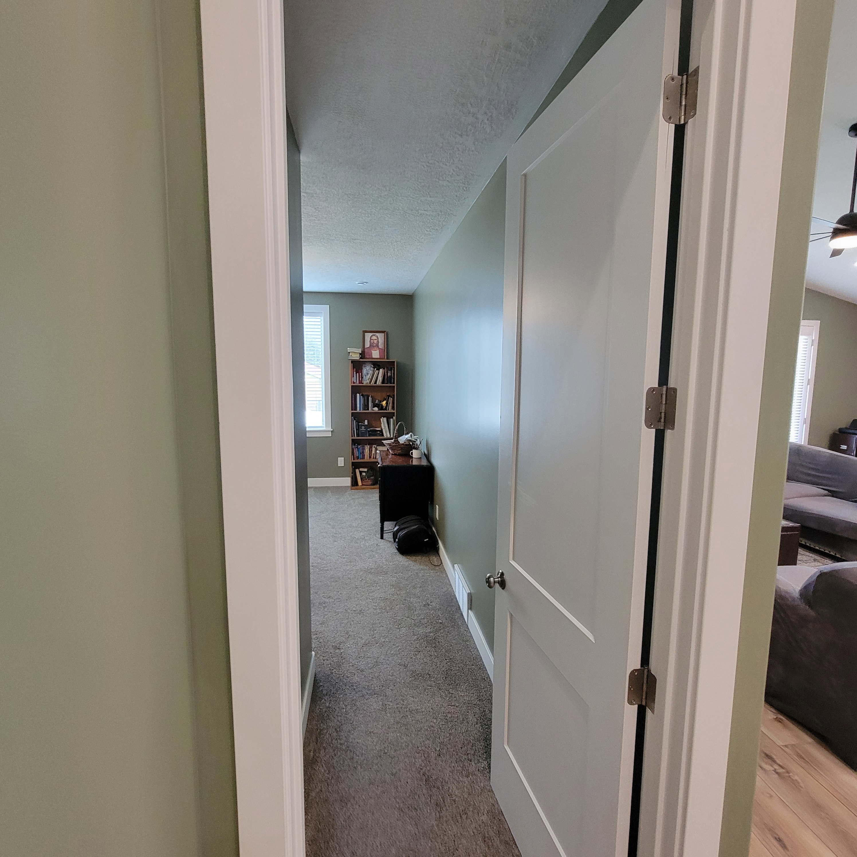 Hallway featuring light green painted walls, white trim, and carpet flooring