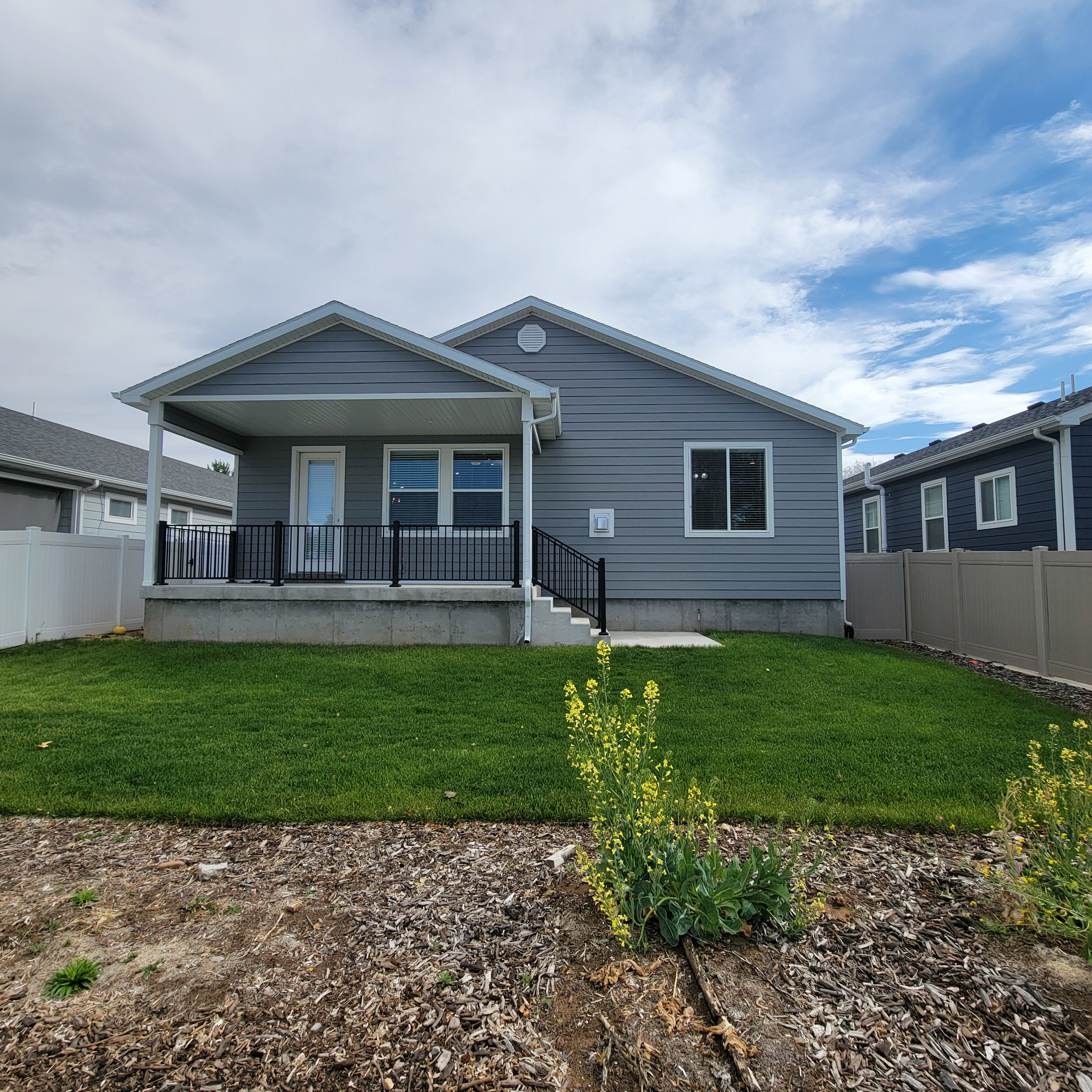 Rear exterior featuring a covered patio with black railings, gray siding, and a manicured lawn