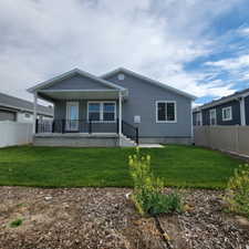 Rear exterior featuring a covered patio with black railings, gray siding, and a manicured lawn