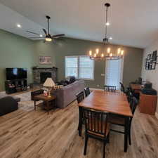 Open-concept living and dining area featuring vaulted ceilings, wood-finish flooring, a brick-surround fireplace, and recessed lighting