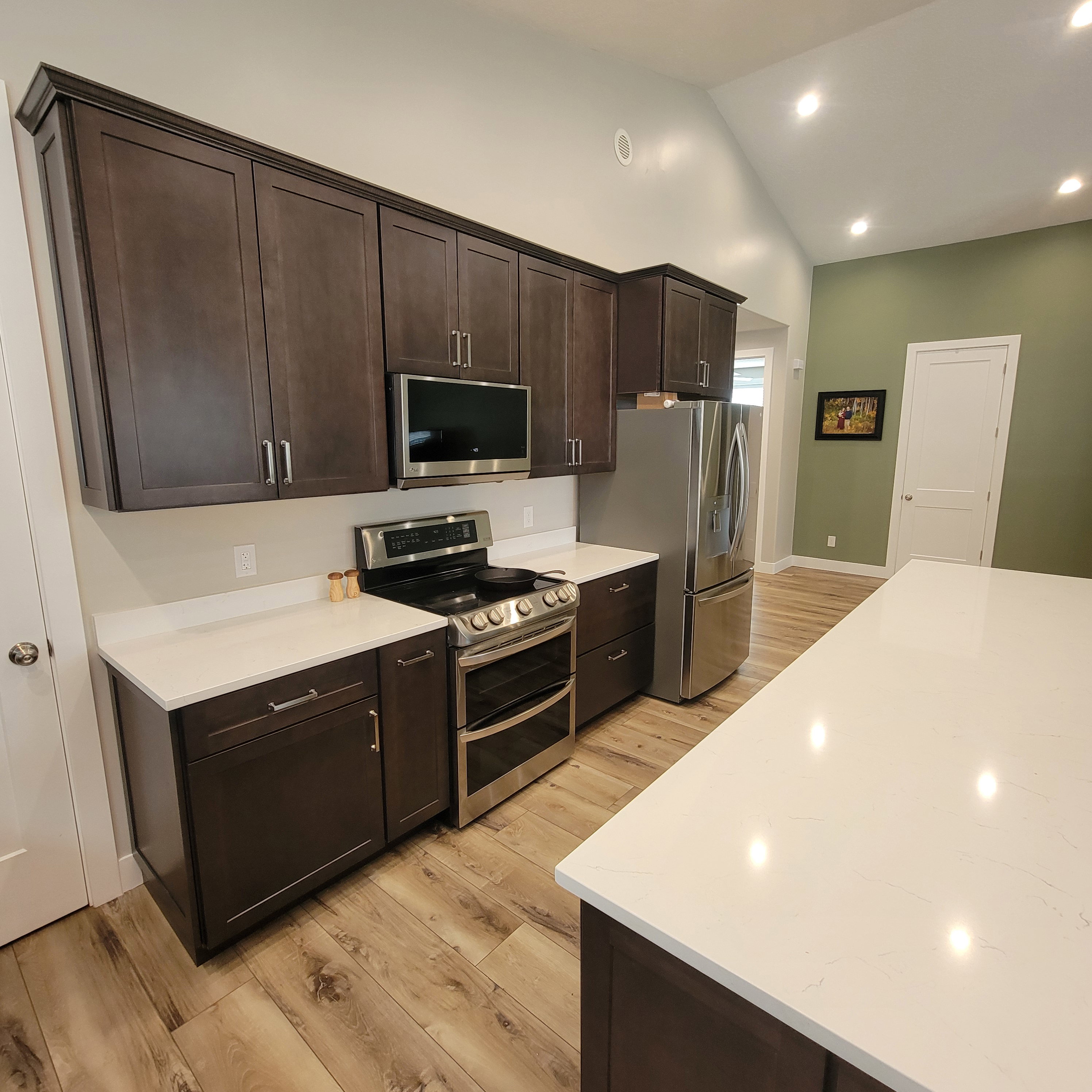 Contemporary kitchen featuring dark wood cabinetry, stainless steel appliances, and white countertops