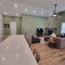 Spacious open-concept living area featuring a stone-clad fireplace, wood-finish flooring, and vaulted ceilings with recessed lighting