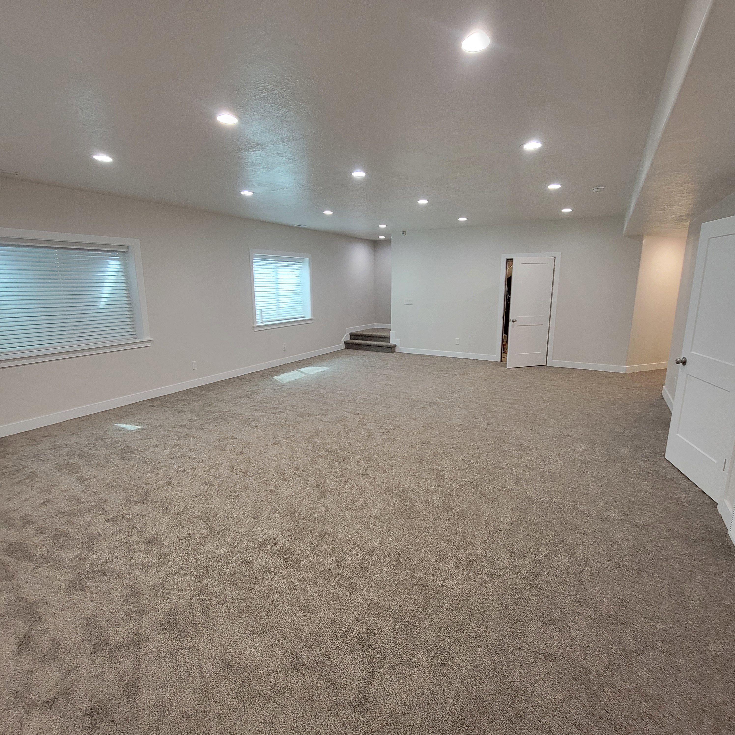 Spacious room featuring new carpeting, recessed lighting, white trim, and multiple windows with blinds